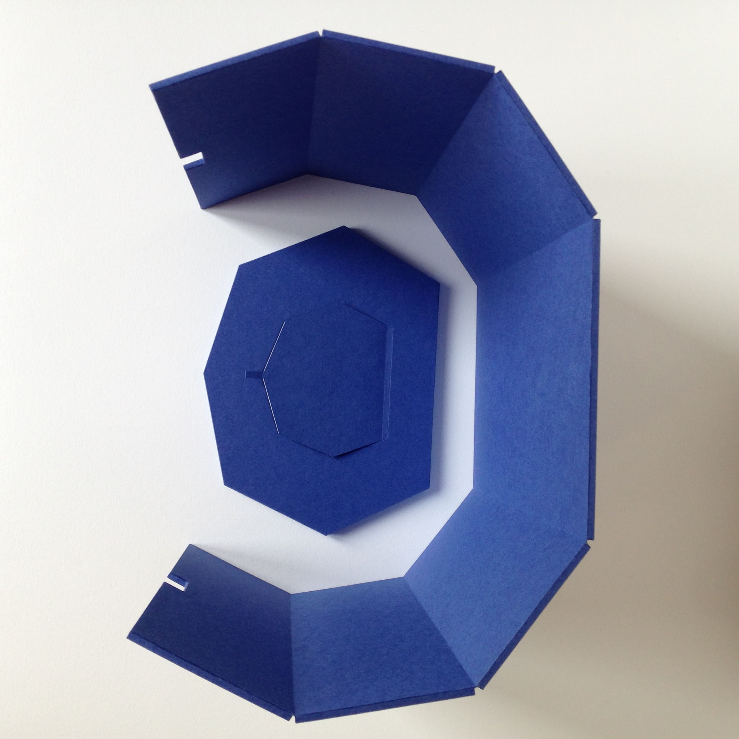 Vue de dessus d'une boîte de conservation facettée en papier bleu. Socle et pan aimantés dissociés.