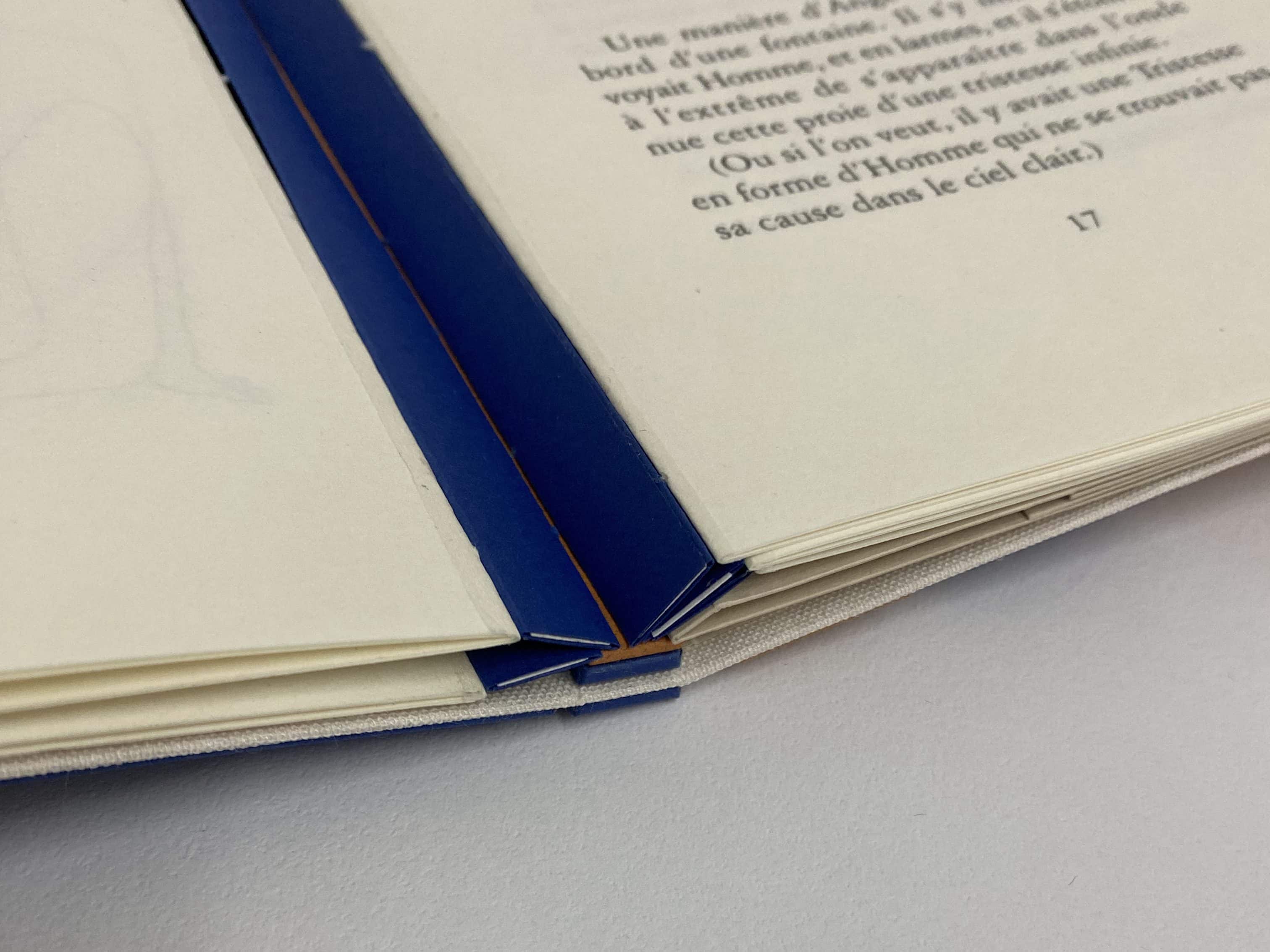 Vue sur les onglets réalisés en papiers colorés, bleu et blanc, cousus sur le dos et les fonds de cahiers