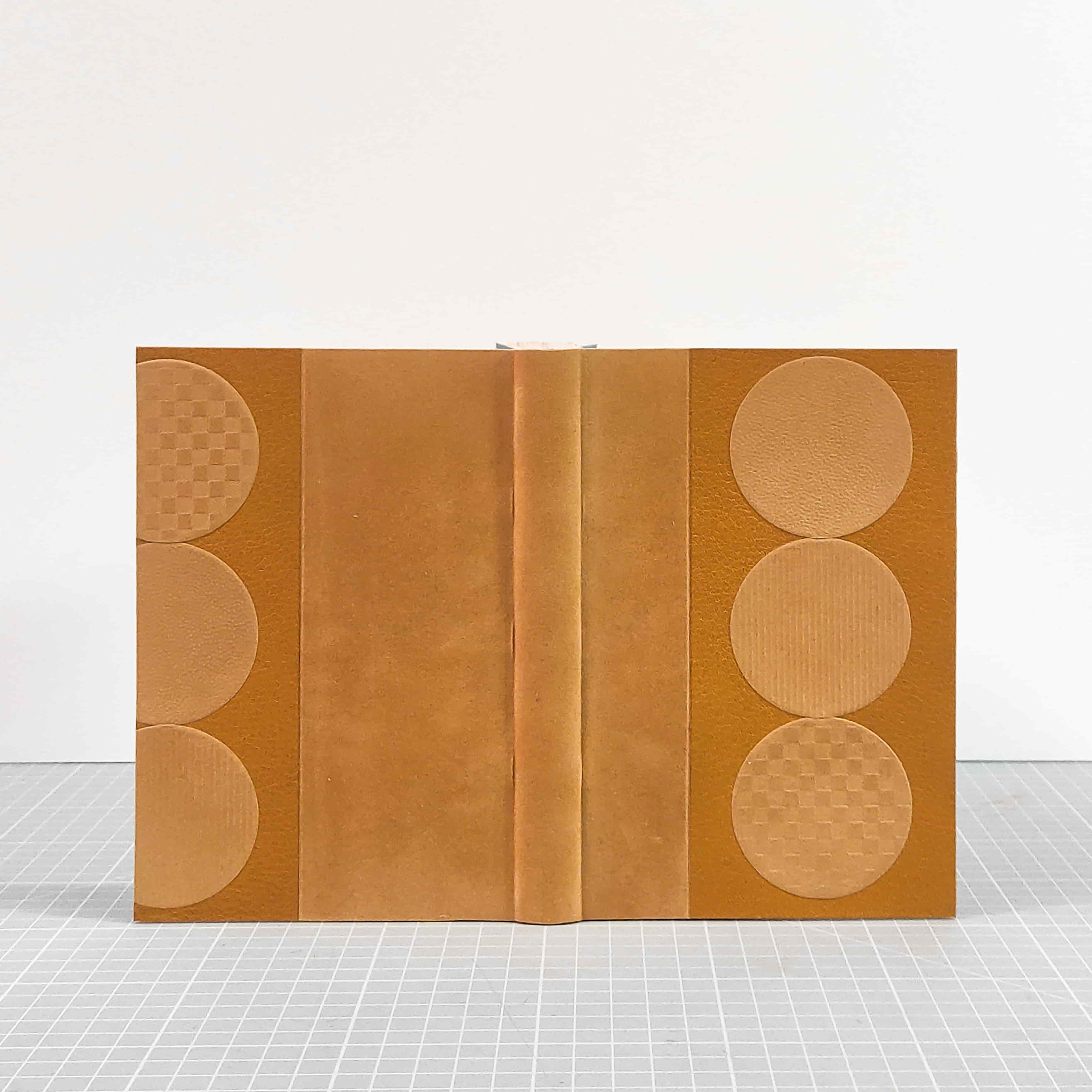 Reliure ouverte proposant une lecture de face des deux plats et du dos, reliure souple, demi cuir et papier velours, éléments mosaïqués en papier velours gaufré